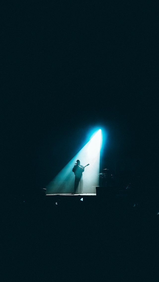 person playing a guitar in the dark with a single spotlight